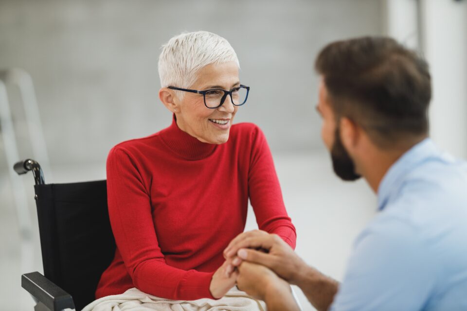 A caregiver holding an older patient's hands during a friendly conversation.