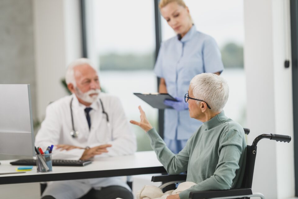 A doctor and nurse reviewing notes with a patient in a bright office.